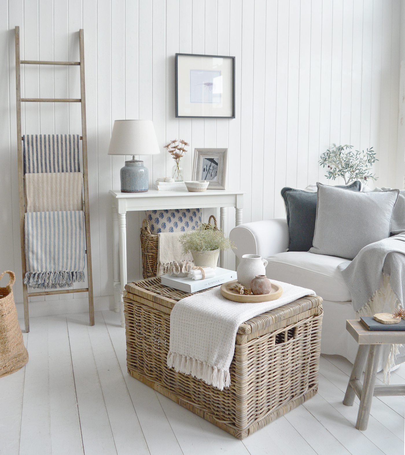 This light-filled living space perfectly captures the timeless elegance of coastal homes and interiors in the Hamptons, with its crisp white panelled walls, soft grey and blue accents, woven textures, and natural materials that create a relaxed yet refined seaside atmosphere.