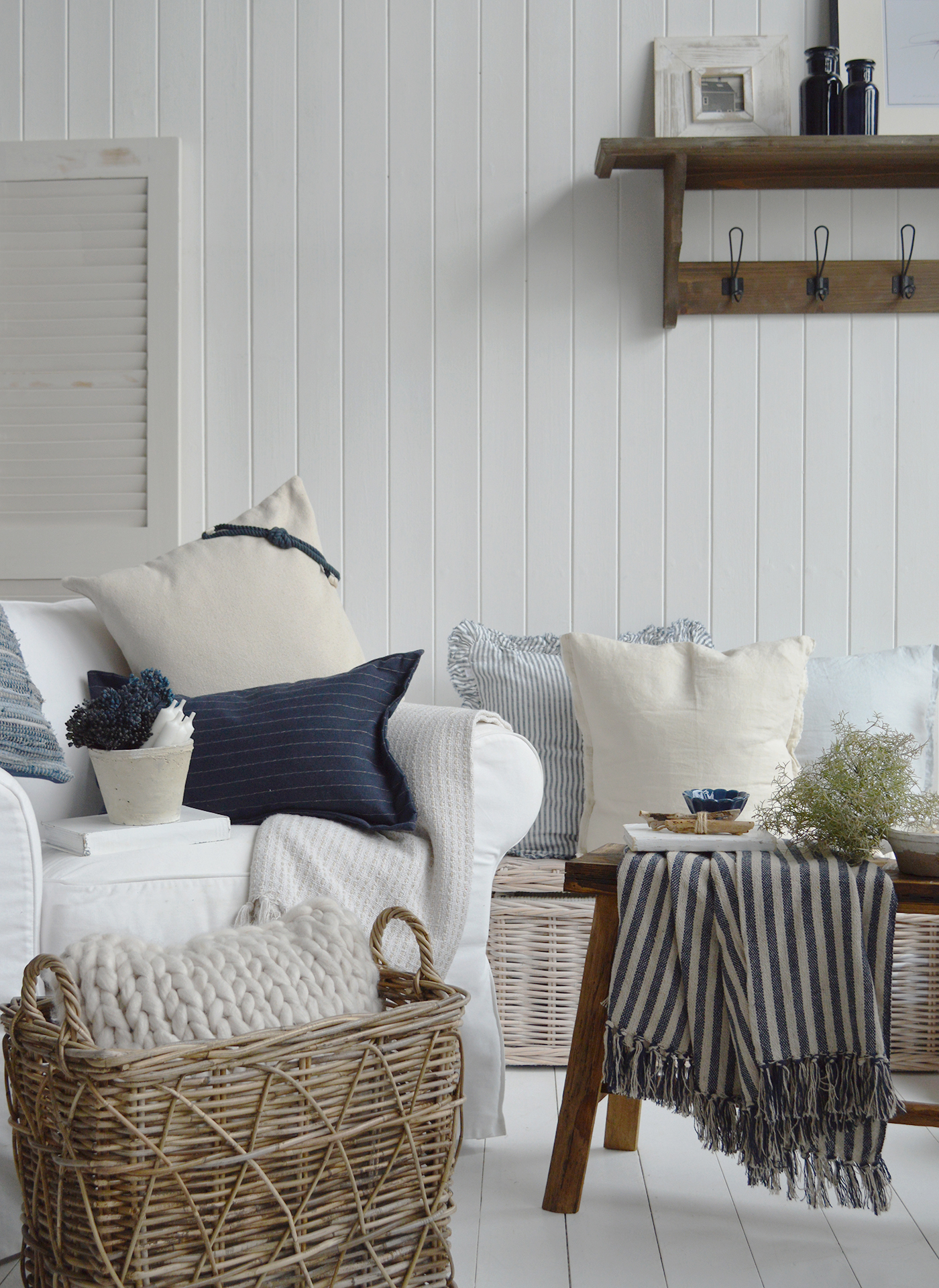 Hamptons-style coastal living room with white slipcover sofa, navy and cream cushions, rattan basket, and striped throw on rustic wooden bench