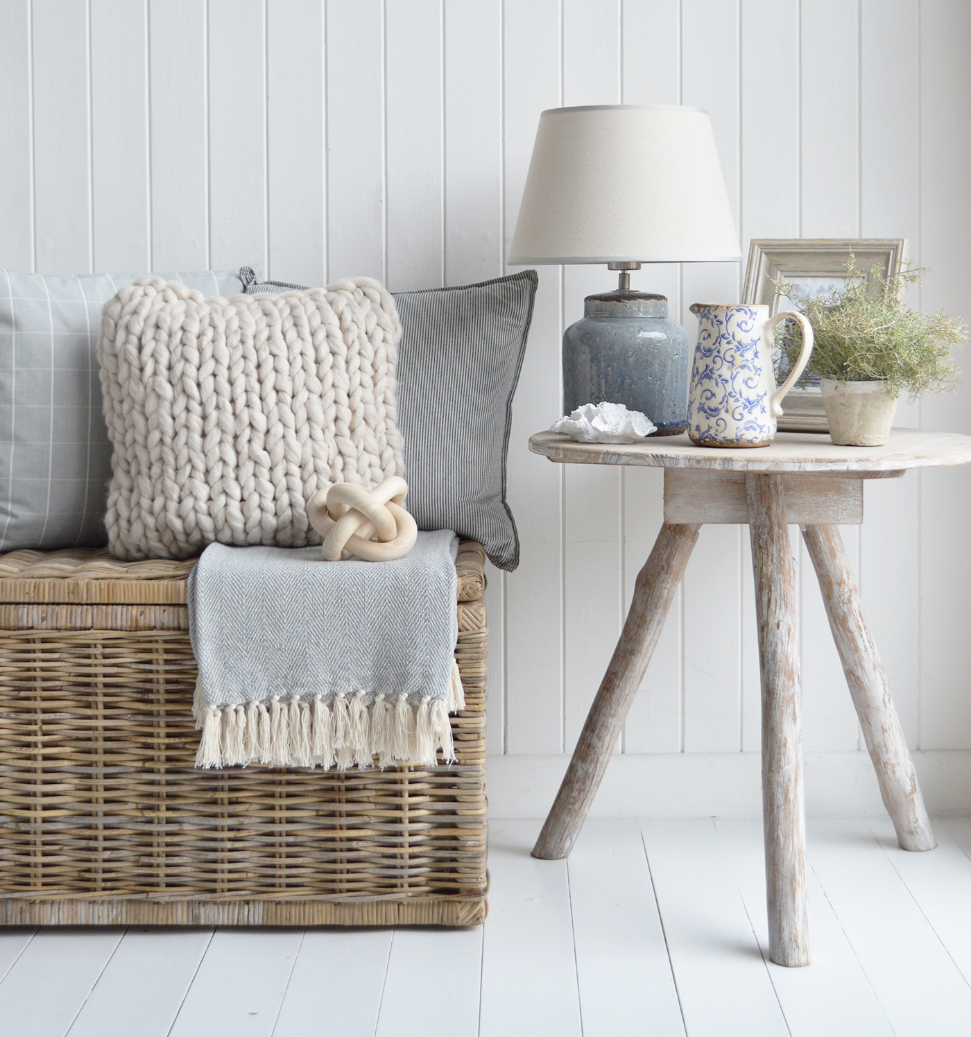 The Mayfair chunky knitted cushion with  
	on the Seaside basket tabkle with the Blue ceramic lamp and Driftwood table