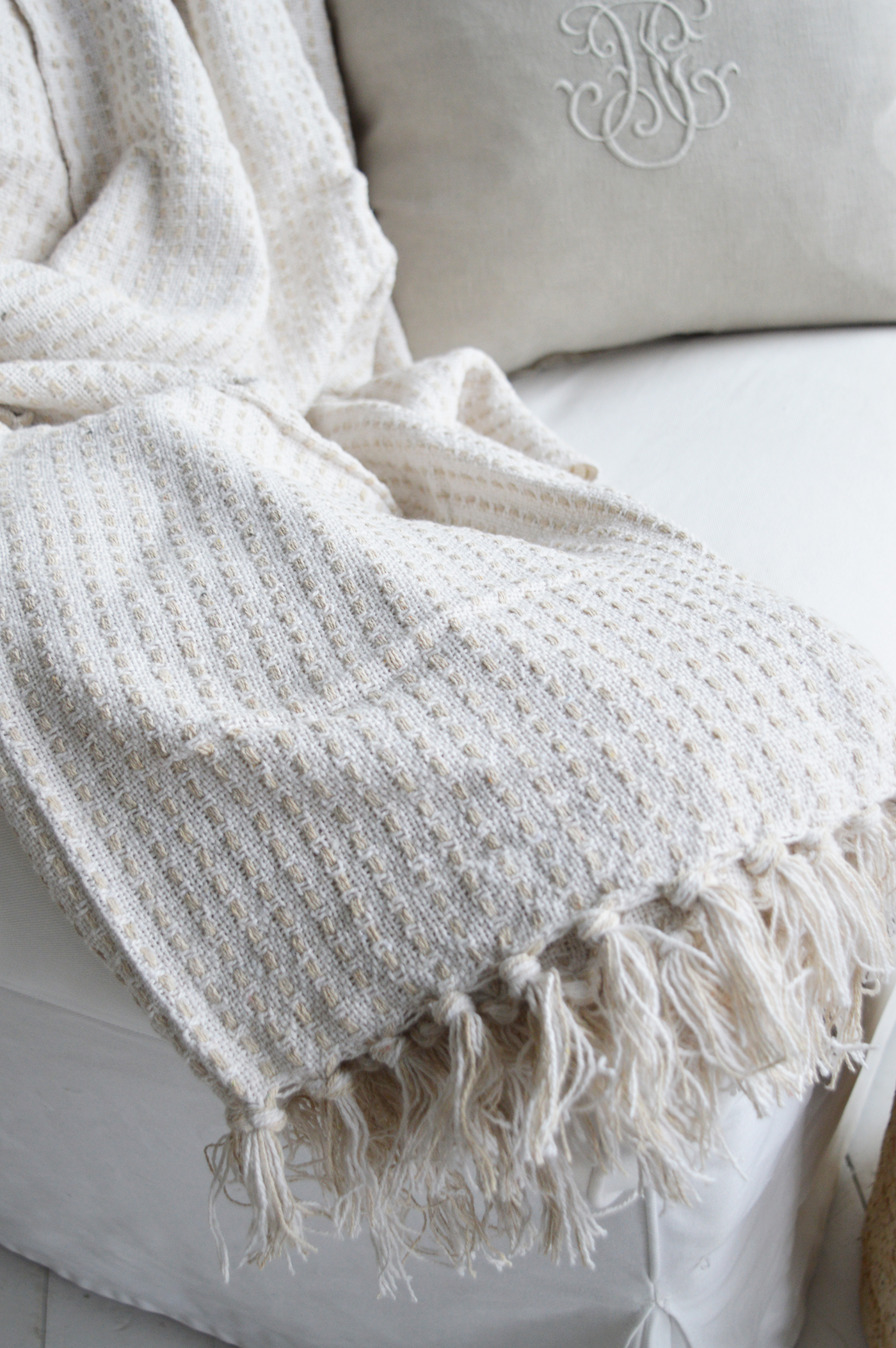 A plush white throw draped over a linen slipcovered sofa adds a touch of relaxed elegance to a coastal Hamptons living room.