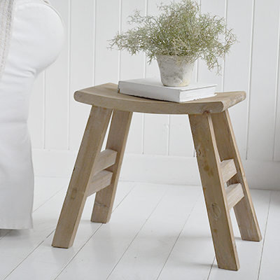 Rustic Pawtucket wooden stool table styled in Hamptons coastal living room with white panel walls. Natural wood stool with curved seat used as side table in coastal New England-inspired home