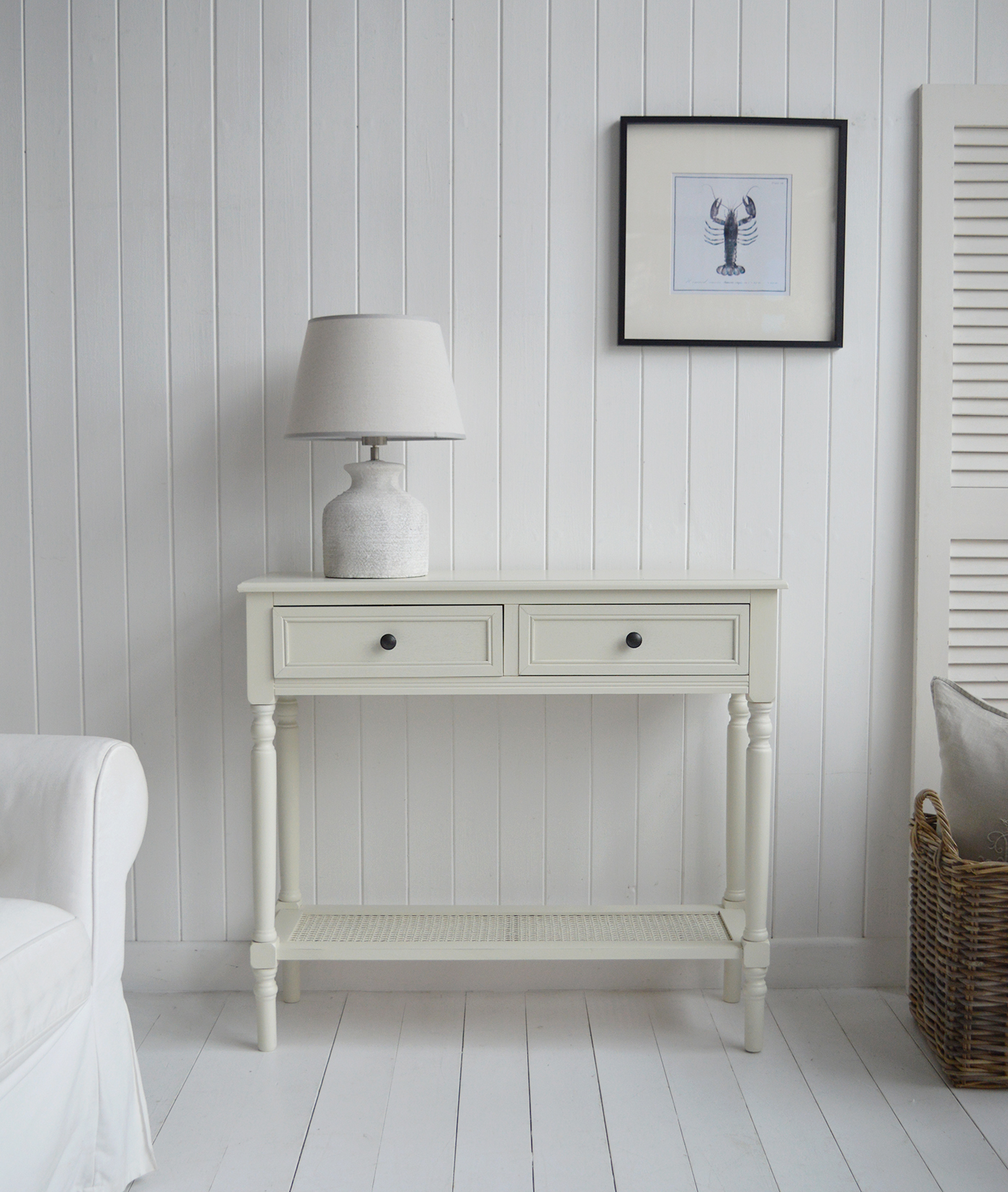 A Hamptons style console table in cream with a rattan shelf and two drawers